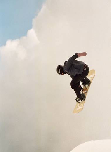 A person jumping with a yellow snowboard with fluffy clouds in the background.
