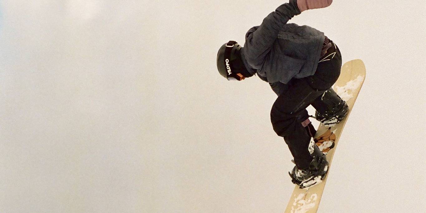 A snowboarder grabs their yellow snowboard mid-air.
