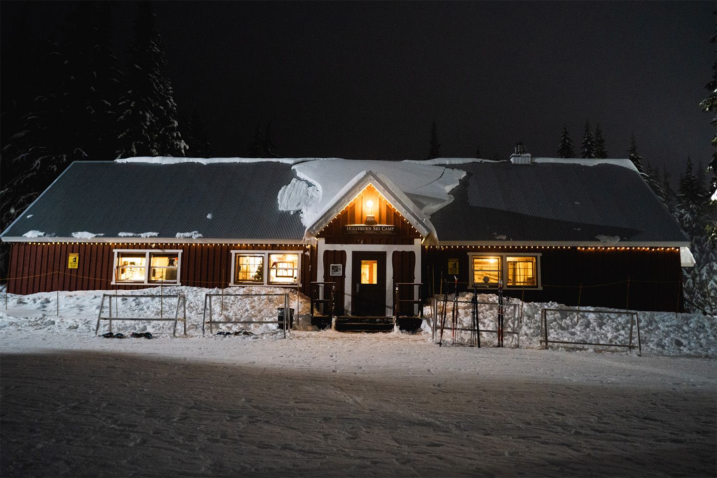 A red building at night with snow on the roof and lights glowing.