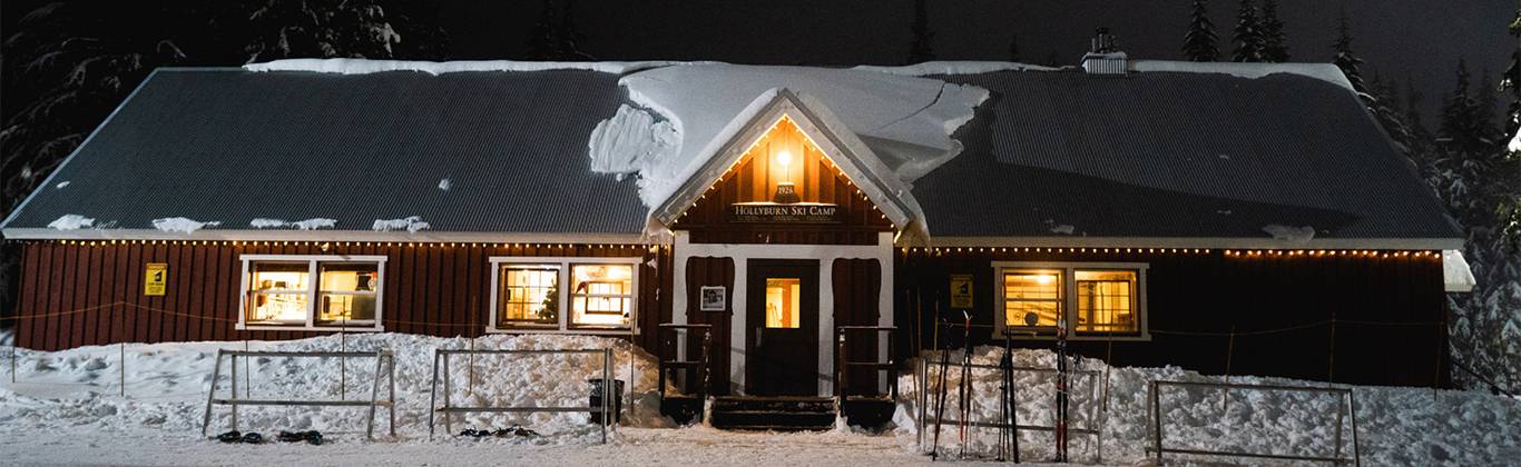 A red building at night with snow on the roof and lights glowing.