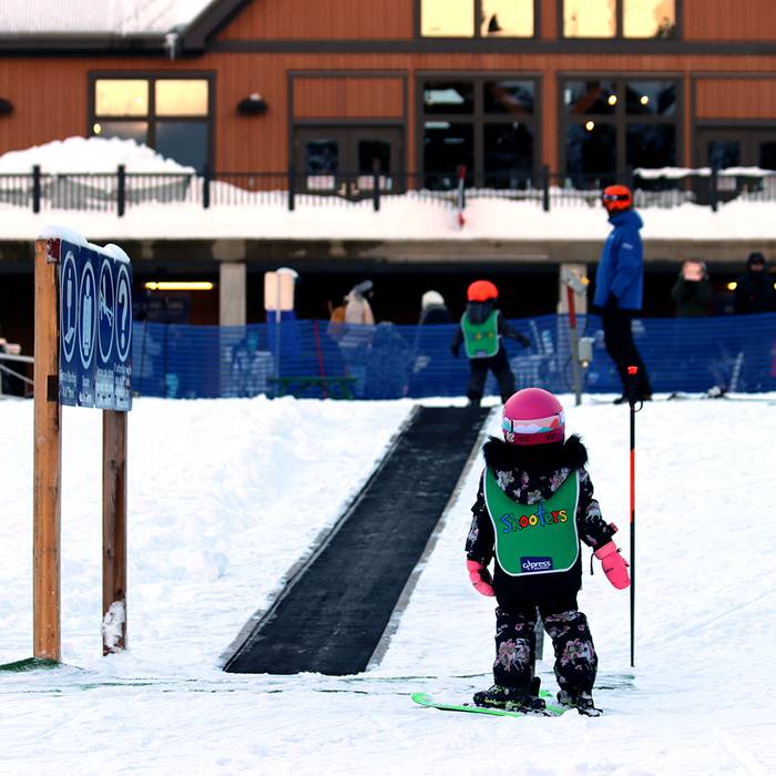 Small child on skis in front of magic carpet.