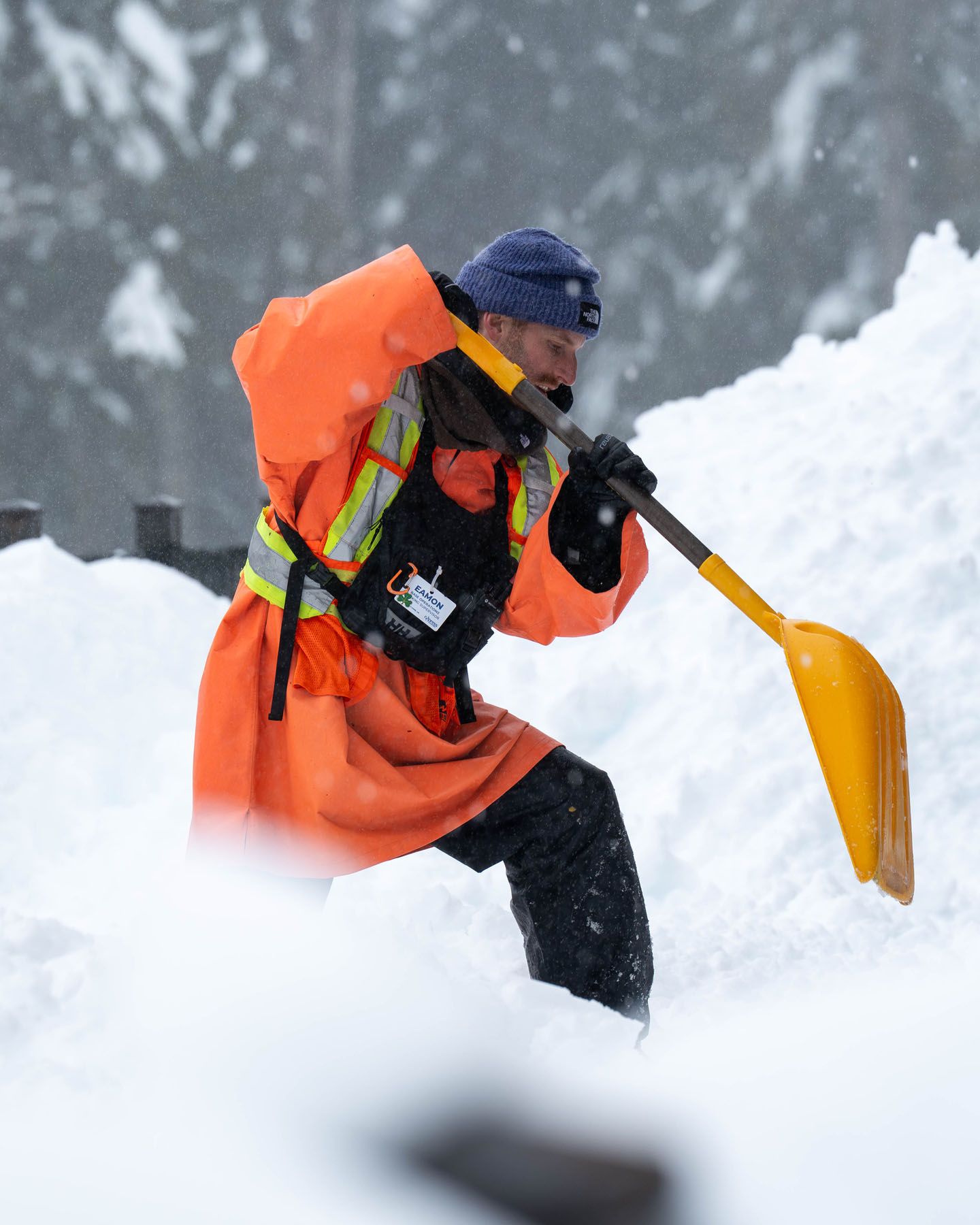 Lift operations staff with an orange uniform shovelling snow.
