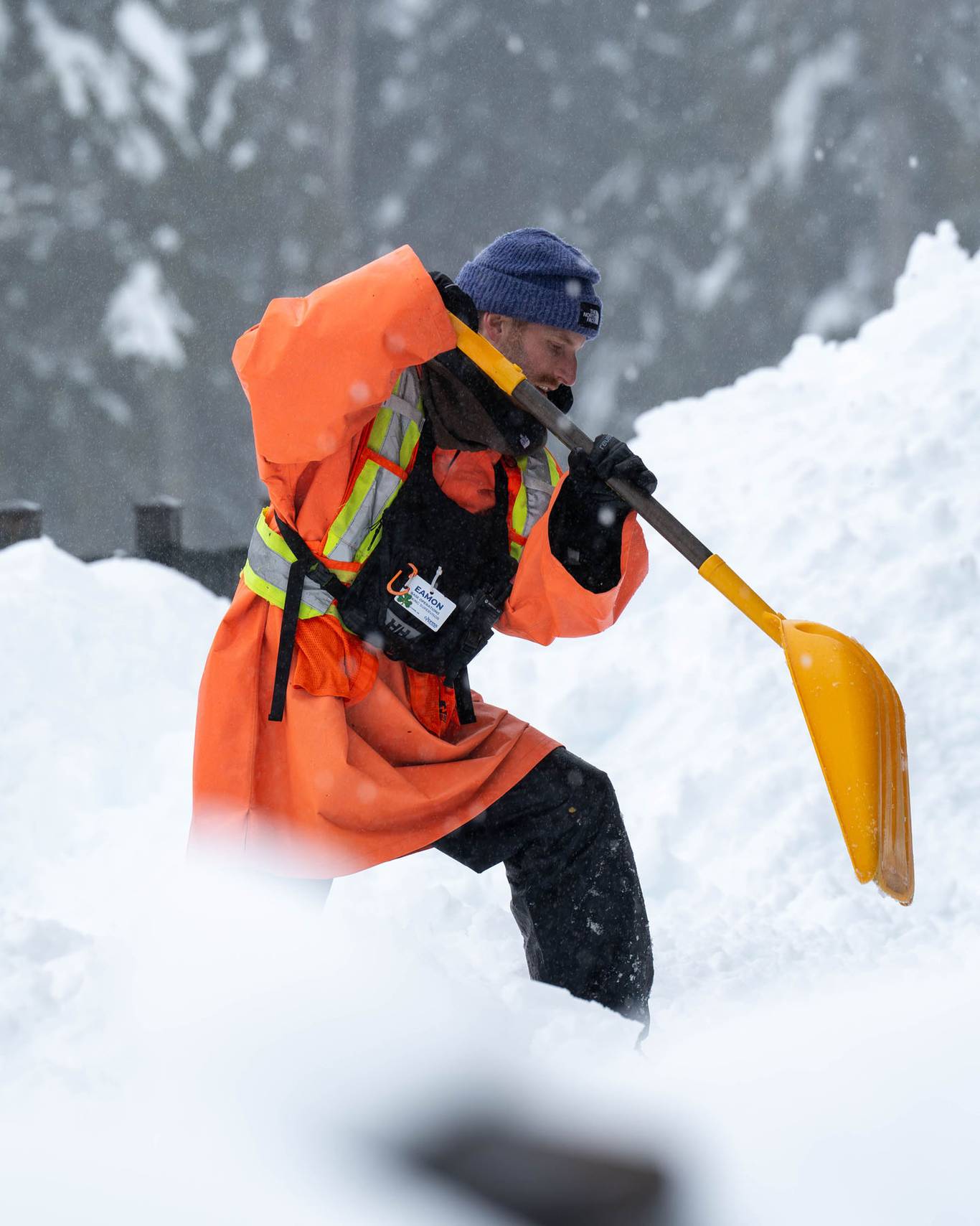 Lift operations staff with an orange uniform shovelling snow.