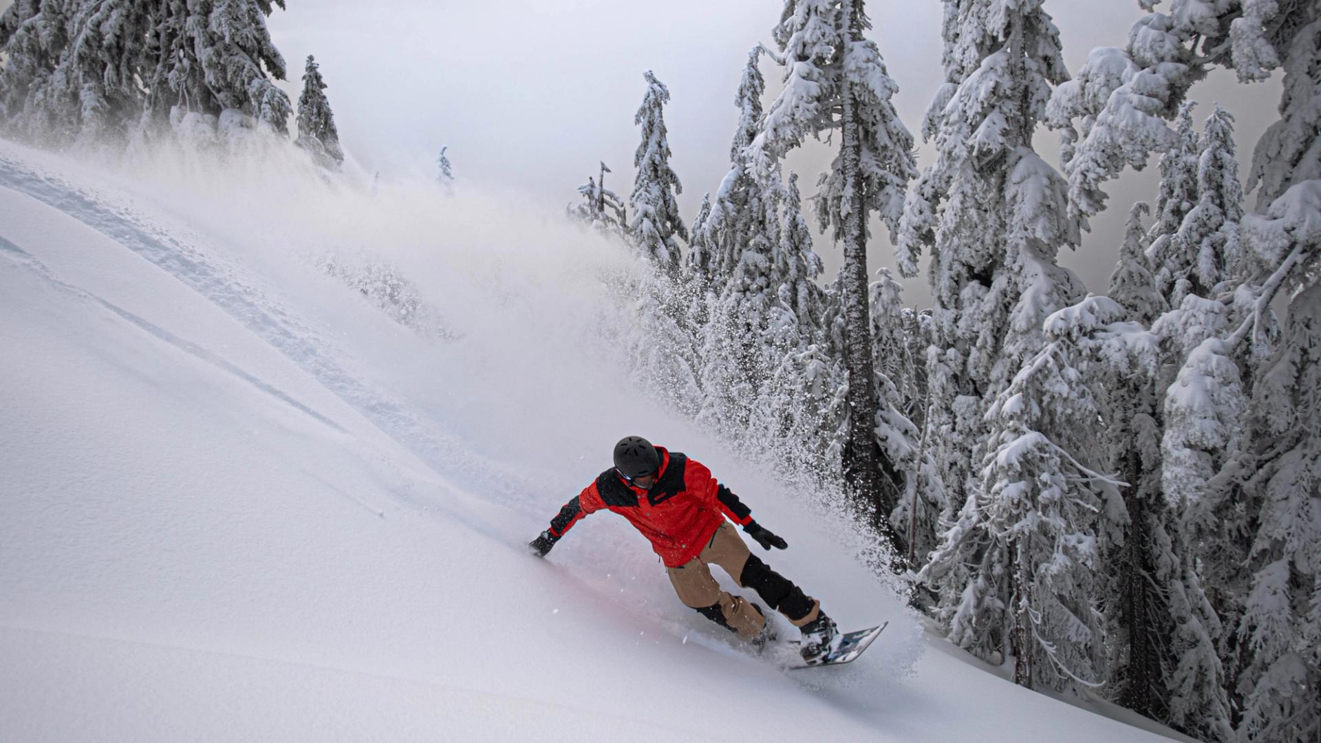 A snowboarder in a red jacket glides through snow on a powder day at Cypress Mountain.