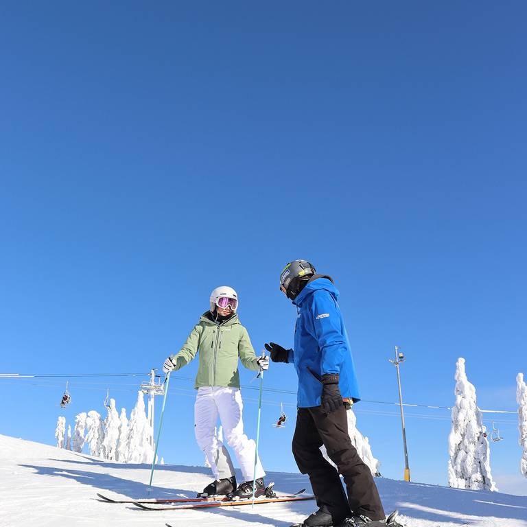 An instructor and adult skier on a bluebird day