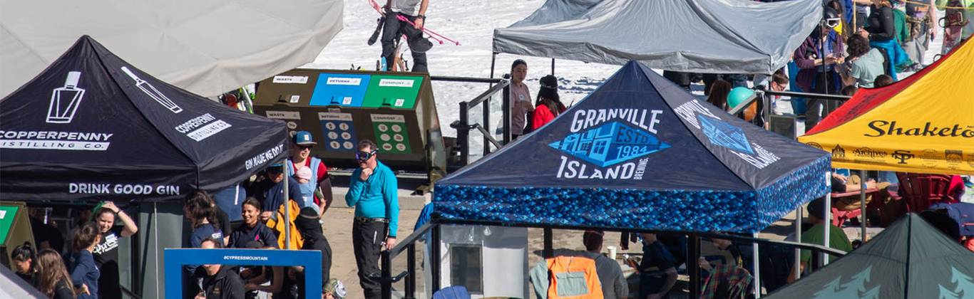 Colourful tents from local breweries and distilleries set up on the outdoor patio at Cypress Mountain on a sunny day.