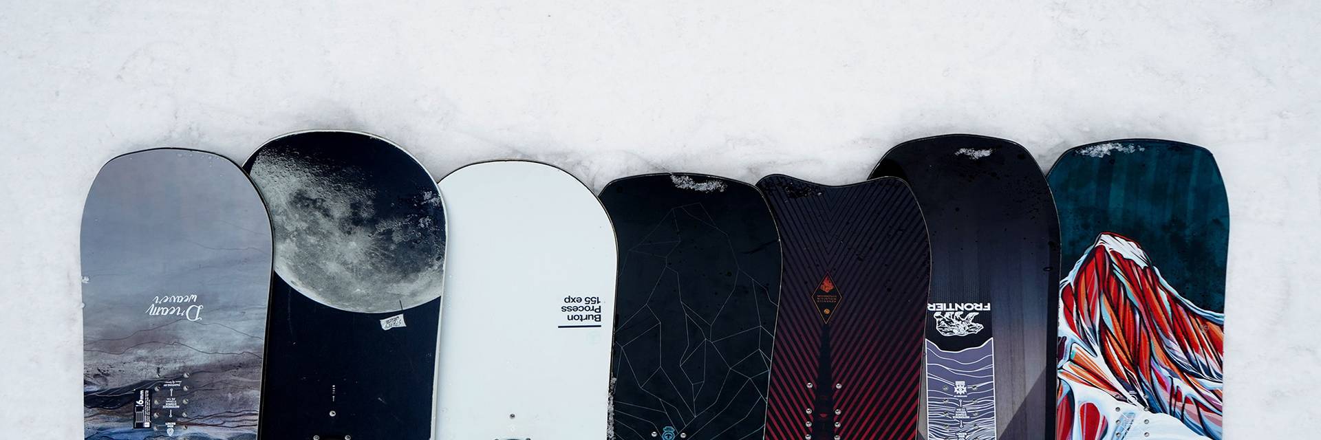Multiple snowboards lined up side-by-side in the snow.