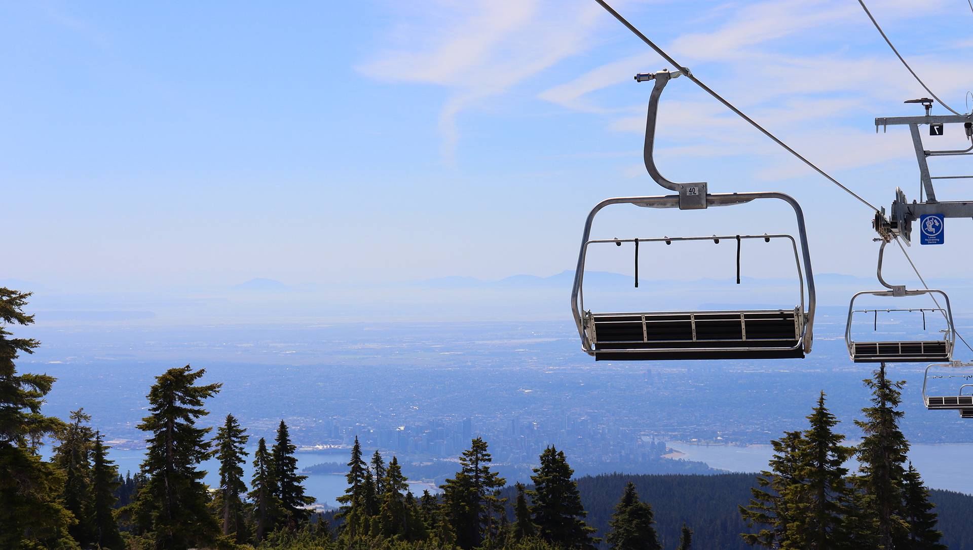 Chairlifts descending the mountain on a sunny day with a view of Vancouver.