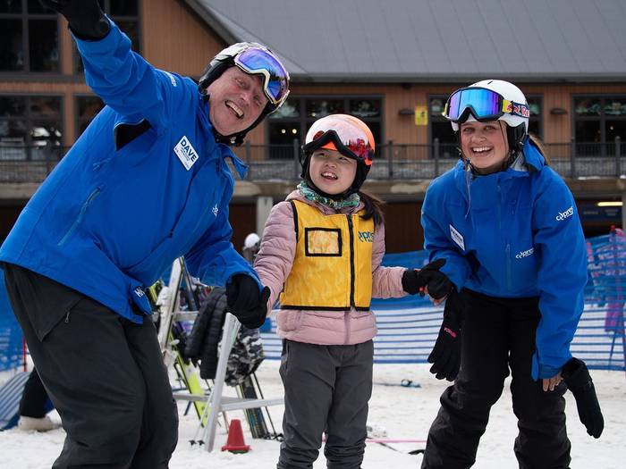Two instructors posing with a child on skis.