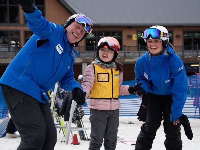 Two instructors posing with a child on skis.