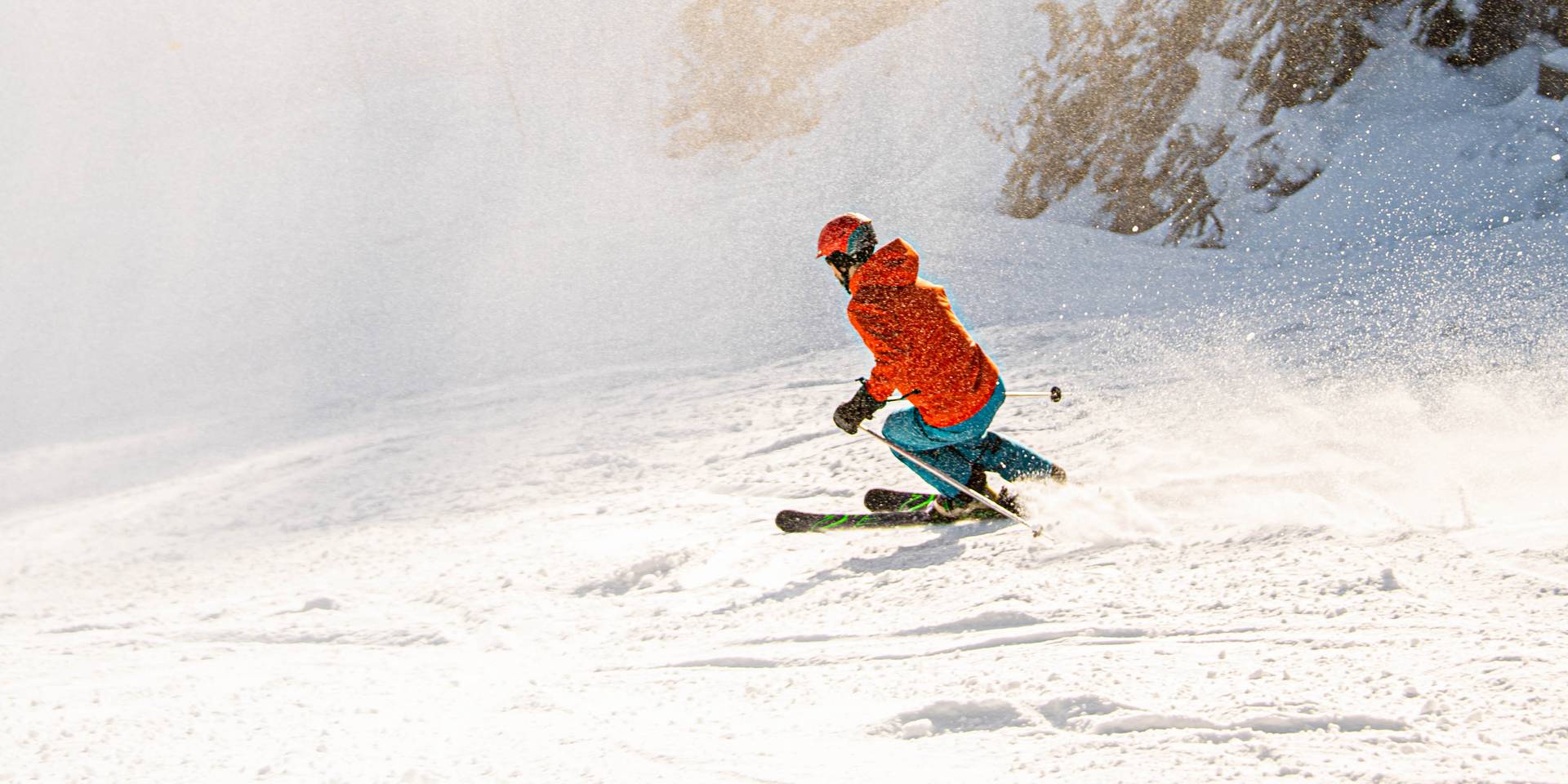 A man in a red jacket skis down a snowy slope on a sunny day.