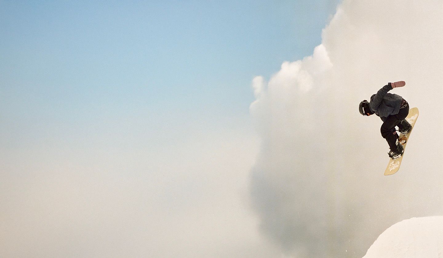 A snowboarder in uniform does a tail grab off a large jump.