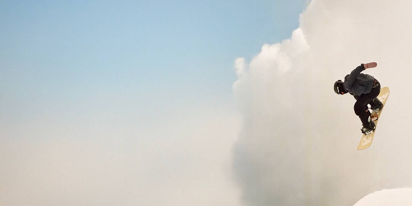 A snowboarder in uniform does a tail grab off a large jump.