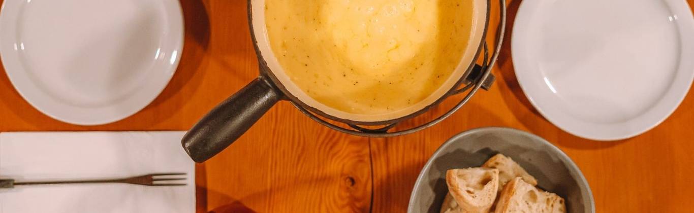 A pot of cheese fondue with bread and mixed vegetables.