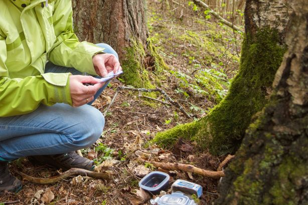 A person in green jacket reading a note from geocaching container.