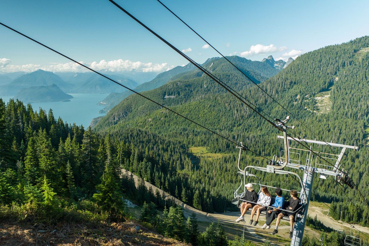 Four people on Lions chairlift looking at the views during summer.