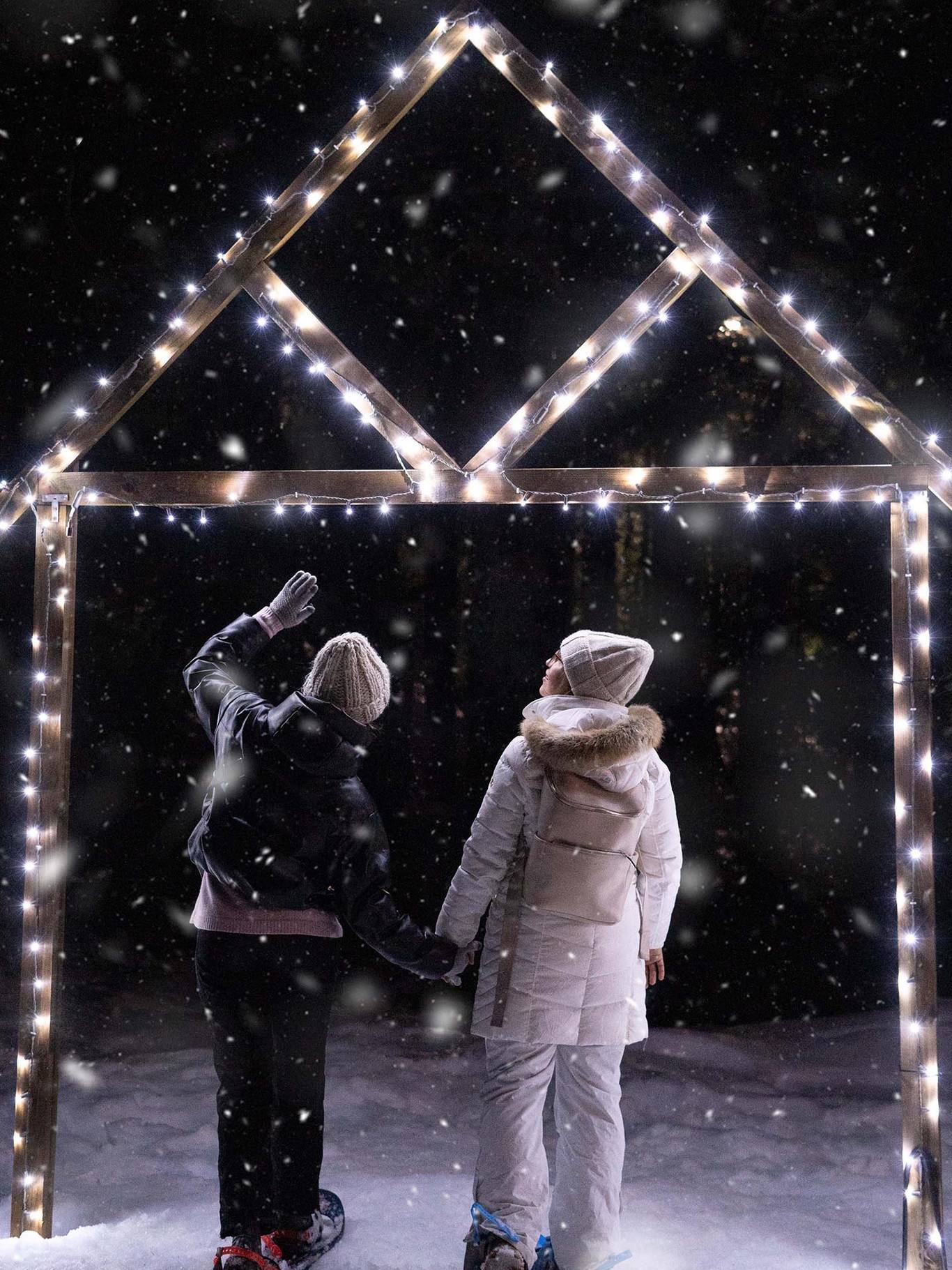 Couple holding hands while snowshoeing at night with lights on an archway.