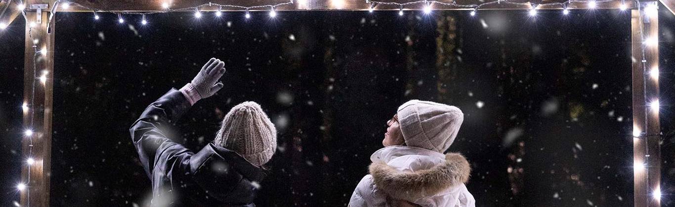 A couple snowshoes to Cypress Mountain's Hollyburn Lodge surrounded by twinkling lights and falling snow