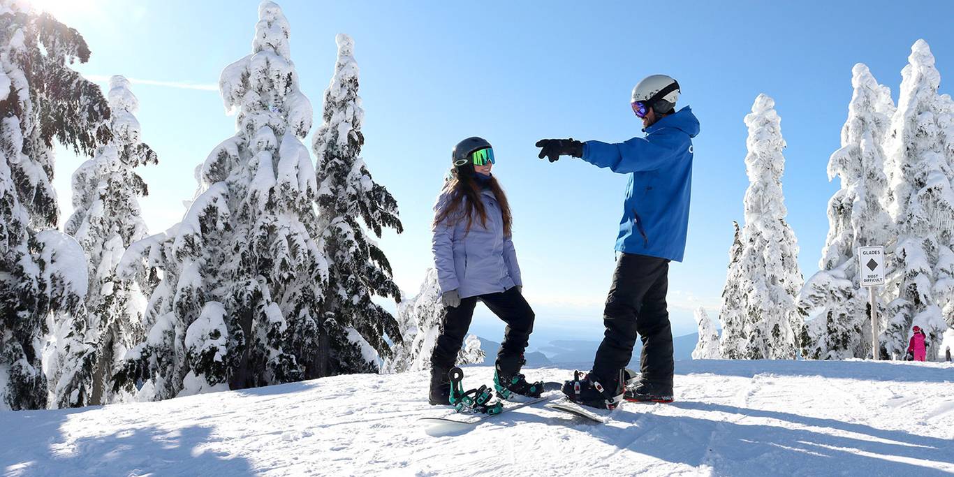 Snowboard instructor teaching a student how to ski a green run on Cypress Mountain resort.