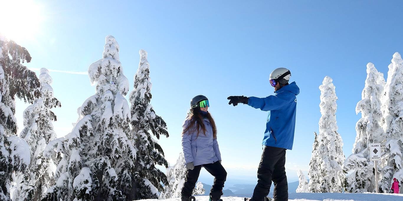 Snowboard instructor teaching a smiling student how to ski a green run.