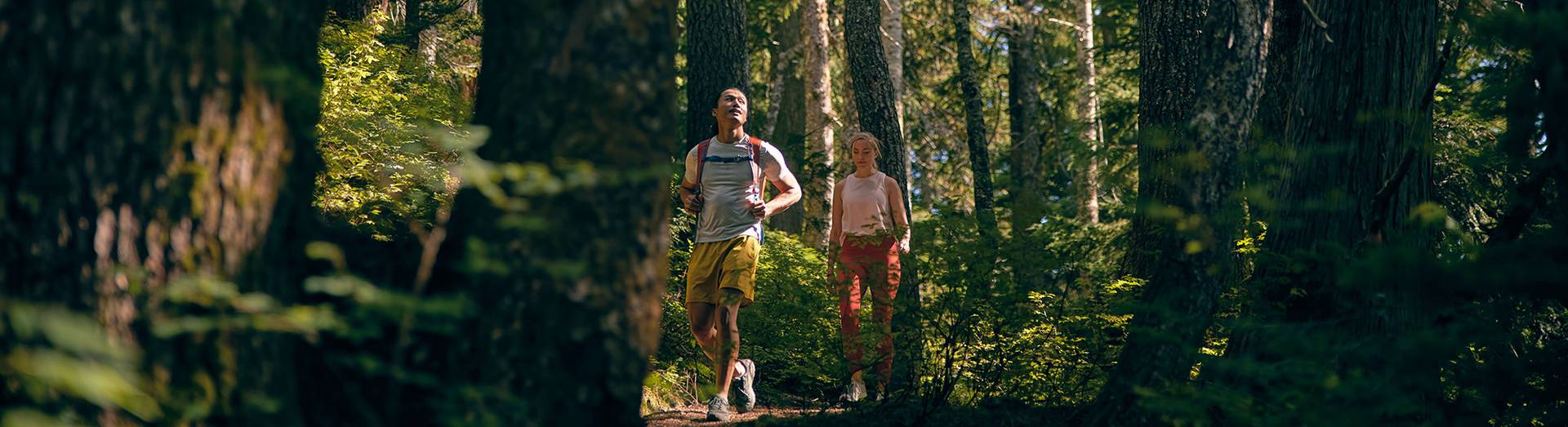 Two friends hiking through the forest wearing brightly colored clothing.