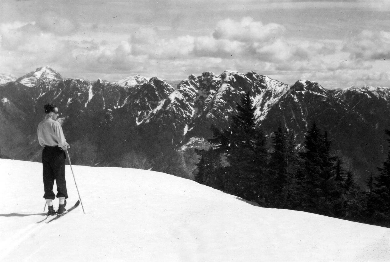 A skier from 1920 looks over the North Shore Mountains while standing on wooden skis.