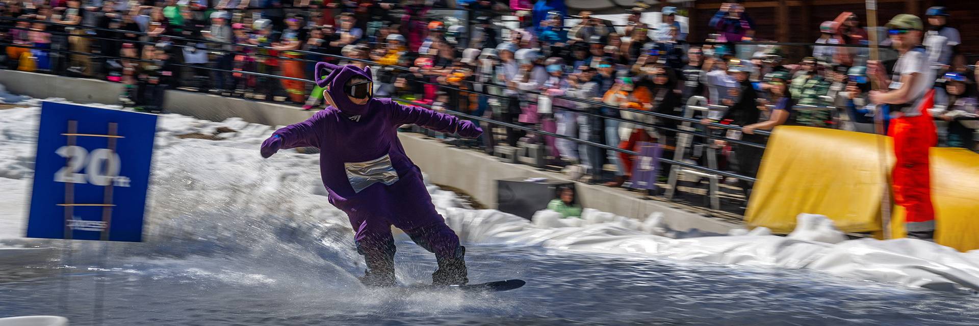 A snowboarder skims across a pool of water in front of a crowd of people on a Cypress Mountain Patio at Slush Cup.