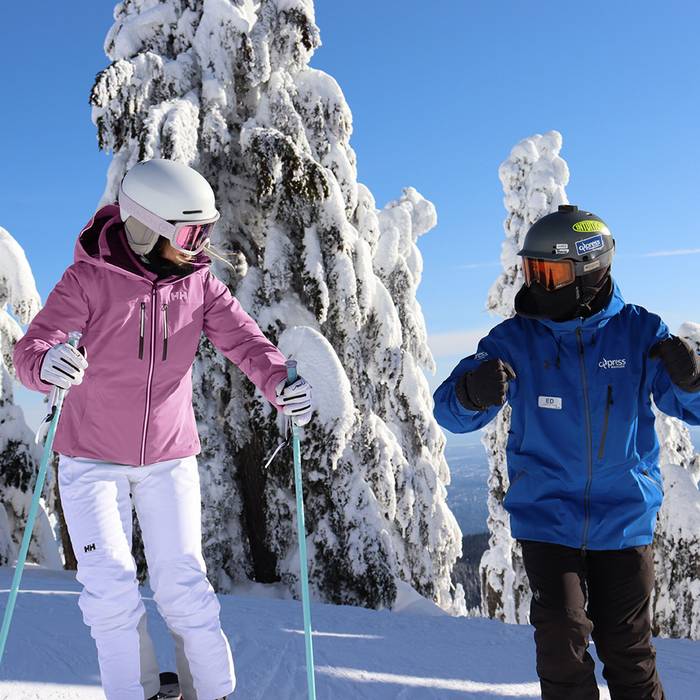 Instructor and adult skier in front of snowy trees