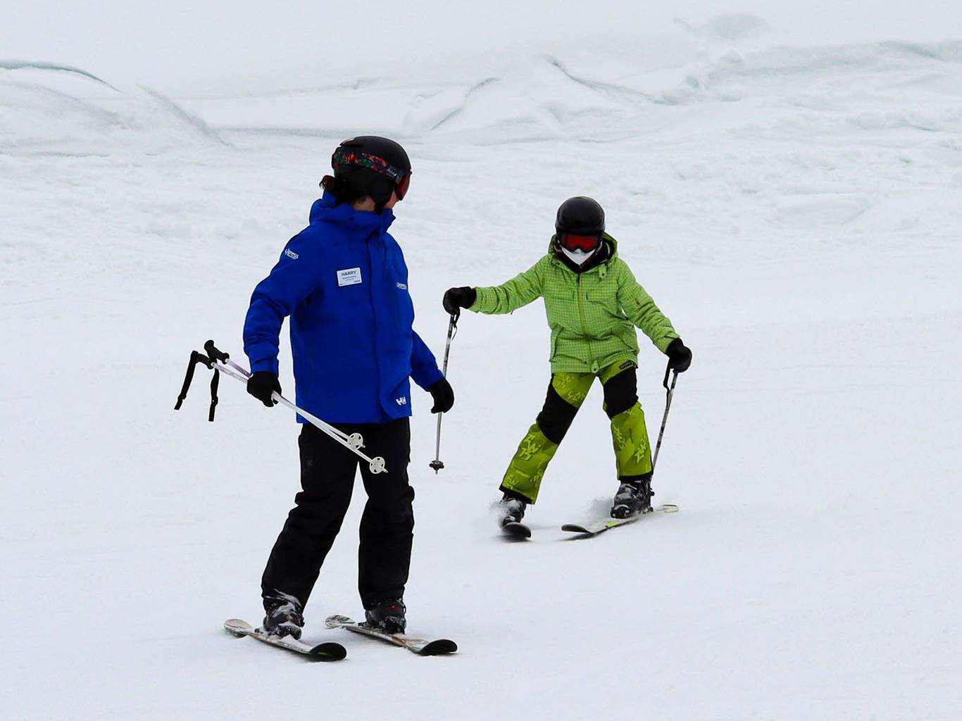 Ski instructor looking back at the child student in green snow outfit.