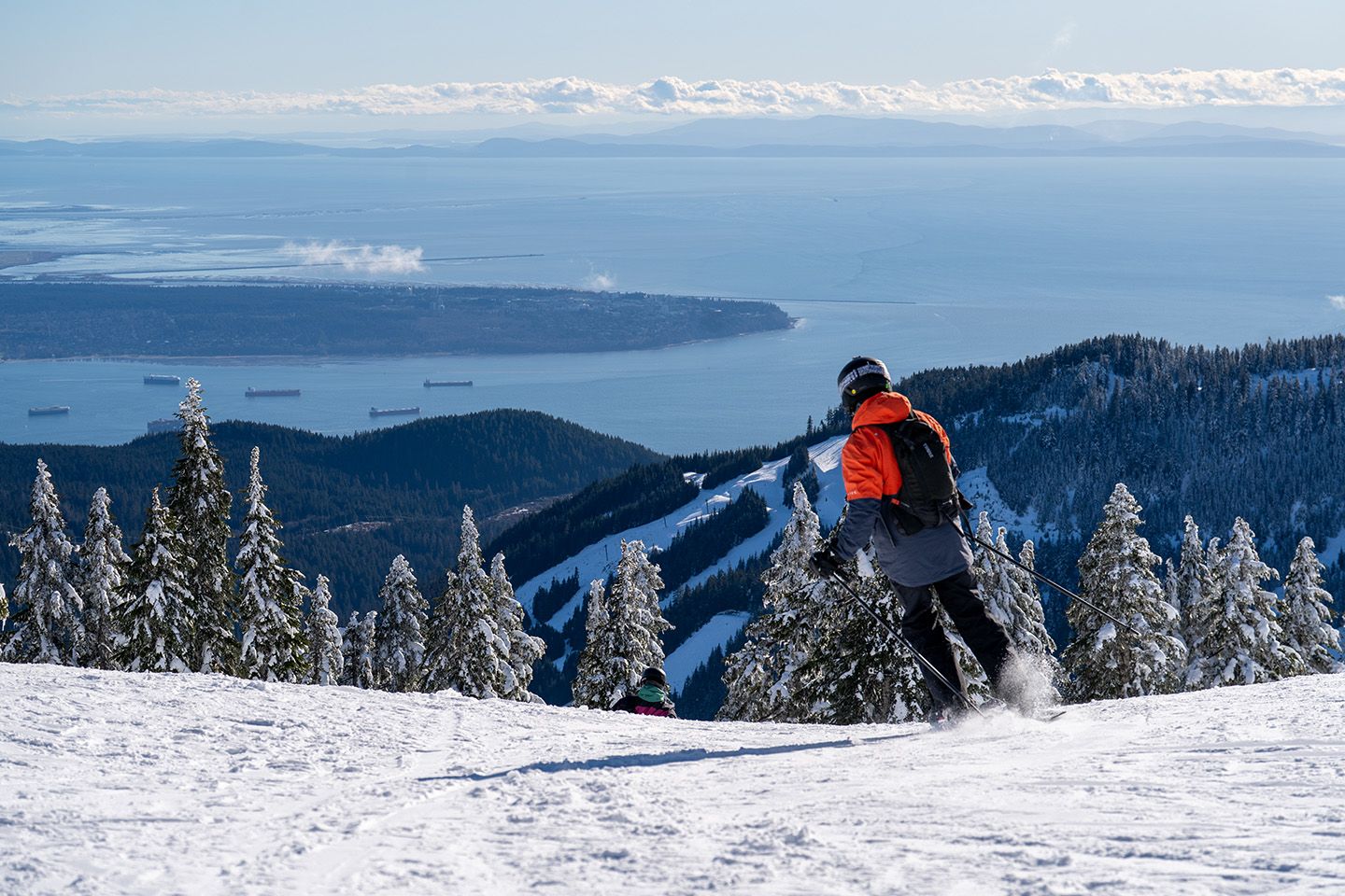 Skier in red jacket with city views on a bluebird day.