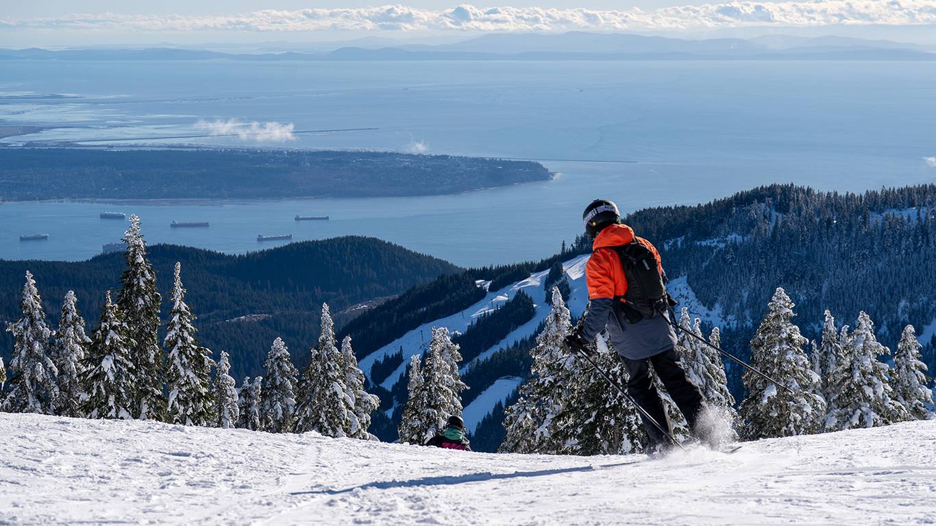 Skier in red jacket with city views on a bluebird day.
