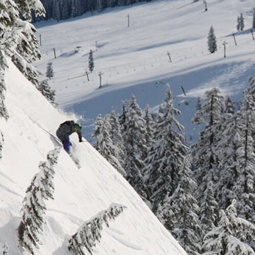 A skier in a black jacket descends a steep ski slope.