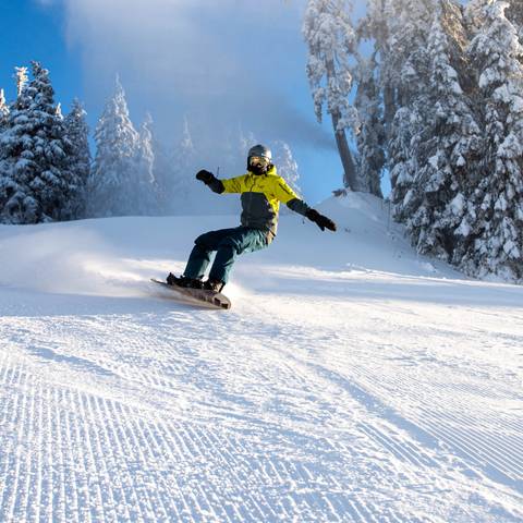 A snowboarder in action, wearing a green jacket on a sunny day.