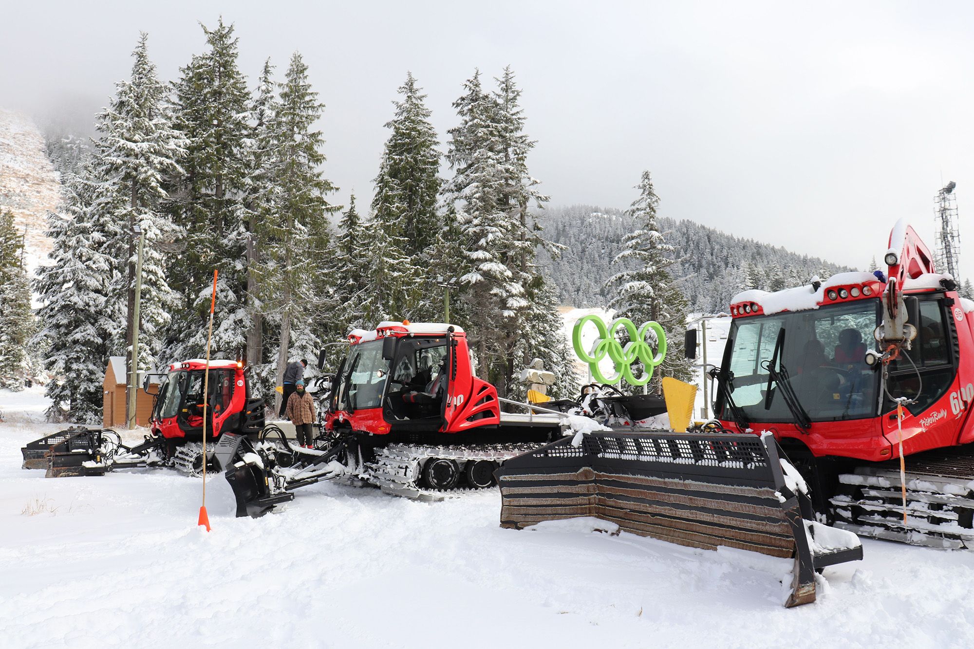 Three snow cats at the bottom of a ski run lined up.