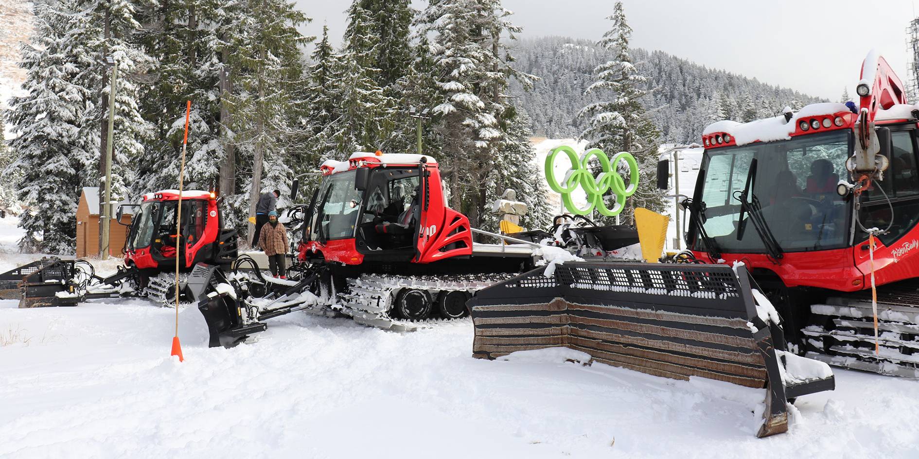 Three snow cats at the bottom of a ski run lined up.