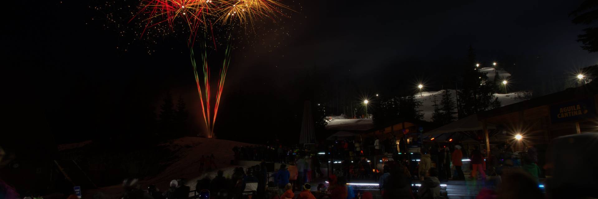 A crowd of people sit on the patio at Cypress Mountain and watch a fireworks display on New Years Eve