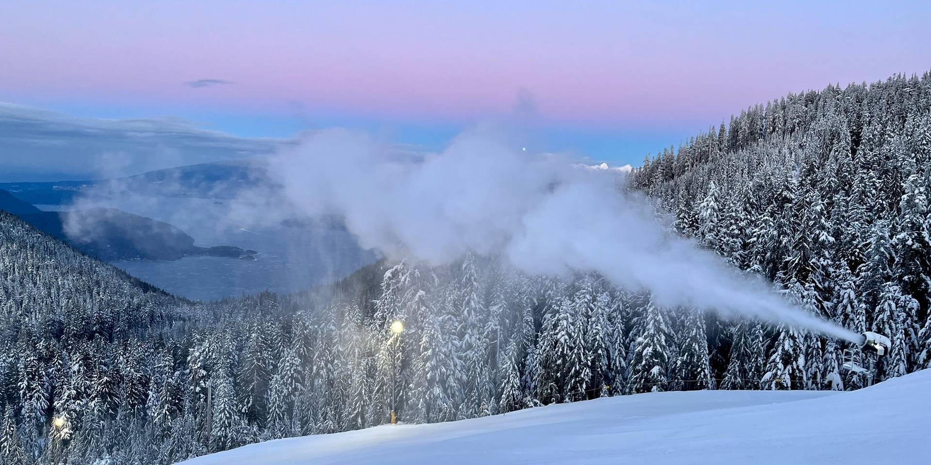 Snow gun spraying snow during sunset.