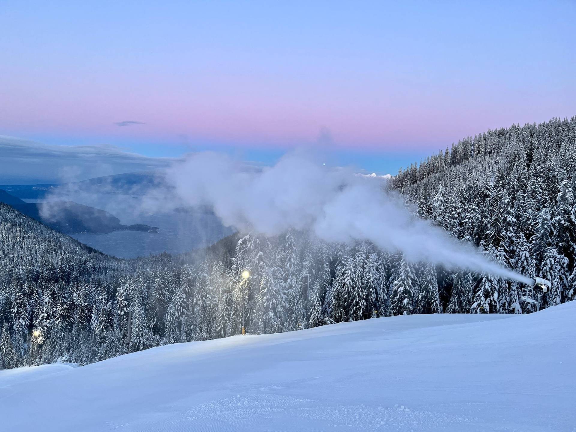 Snow gun spraying snow during sunset.