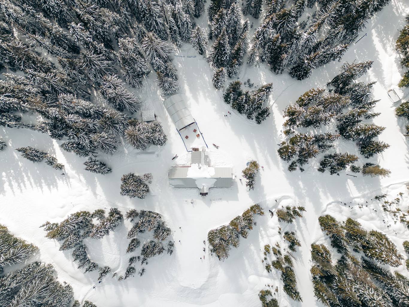 A red lodge in the winter time with guests milling around outside it.