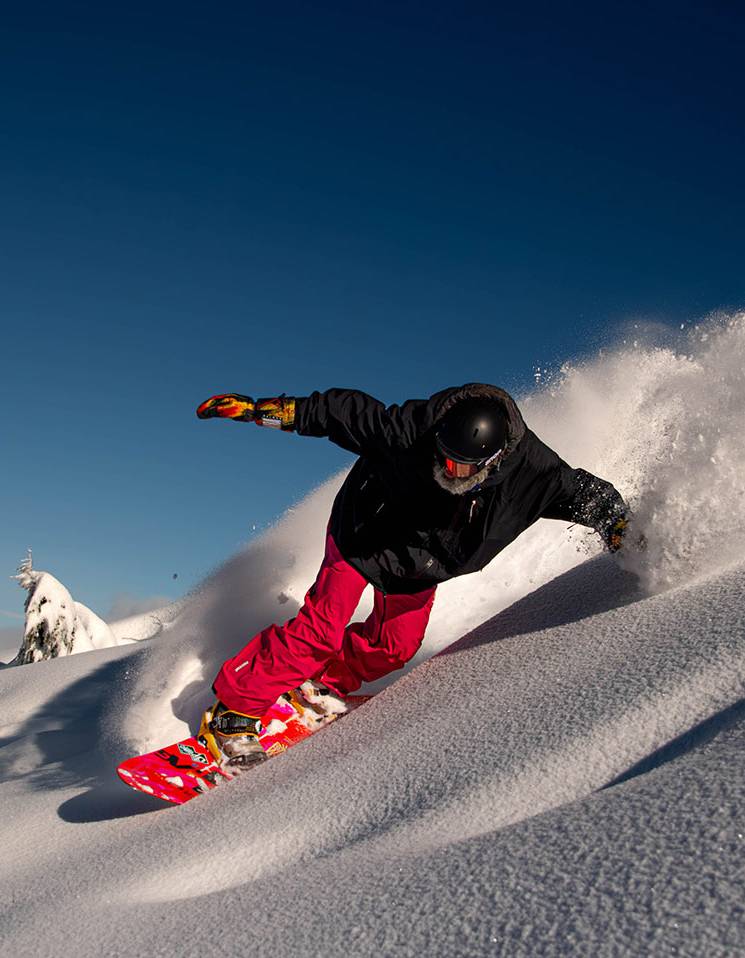 A snowboarder with red pants carving through powder.