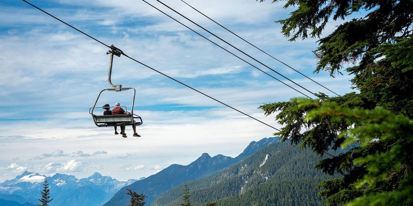 Two people sitting on a chair lift enjoying the view of the mountains.