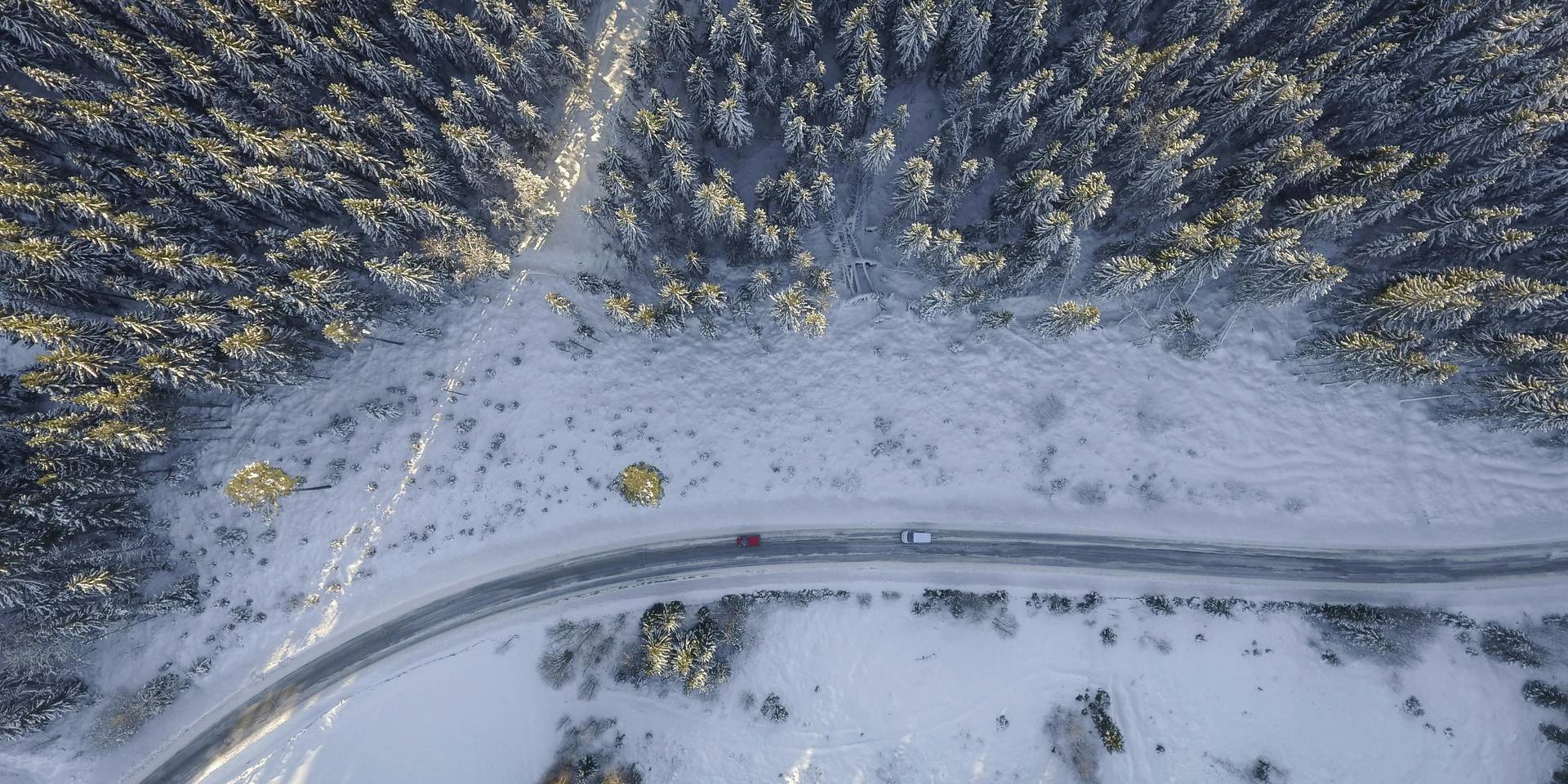 A road winds through a snowy forest as viewed from above.