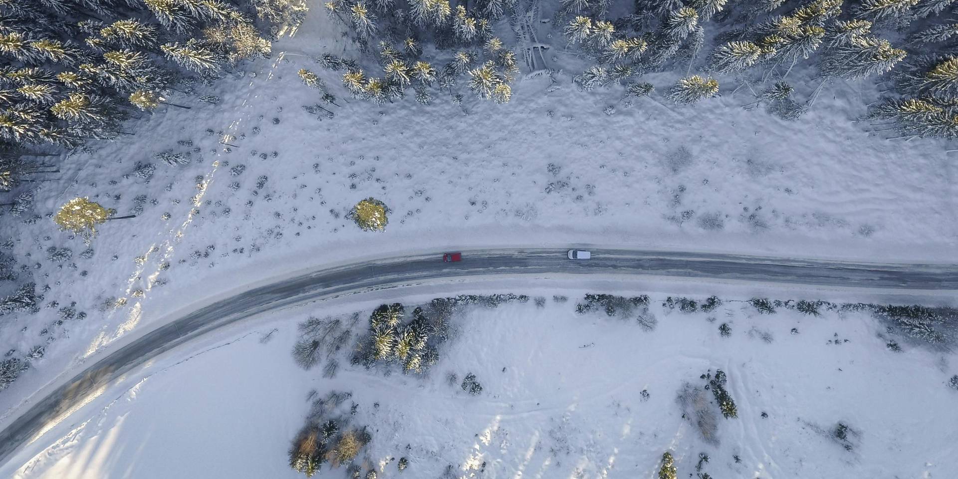 Cypress Bowl Road with two cars on it winds through a snow covered landscape.