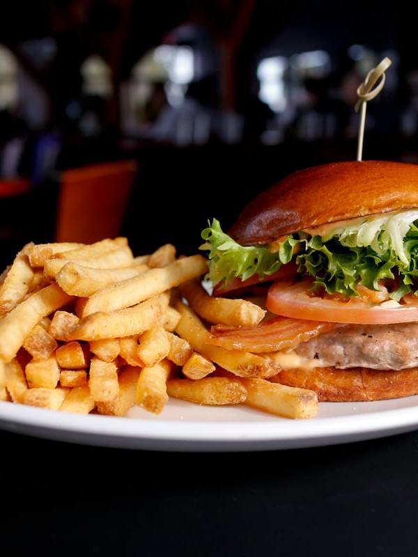 A plate of French fries served with a gourmet burger topped with fresh lettuce, tomato, and onion in a toasted bun, photographed in the cozy dining area of Crazy Raven Bar & Grill.