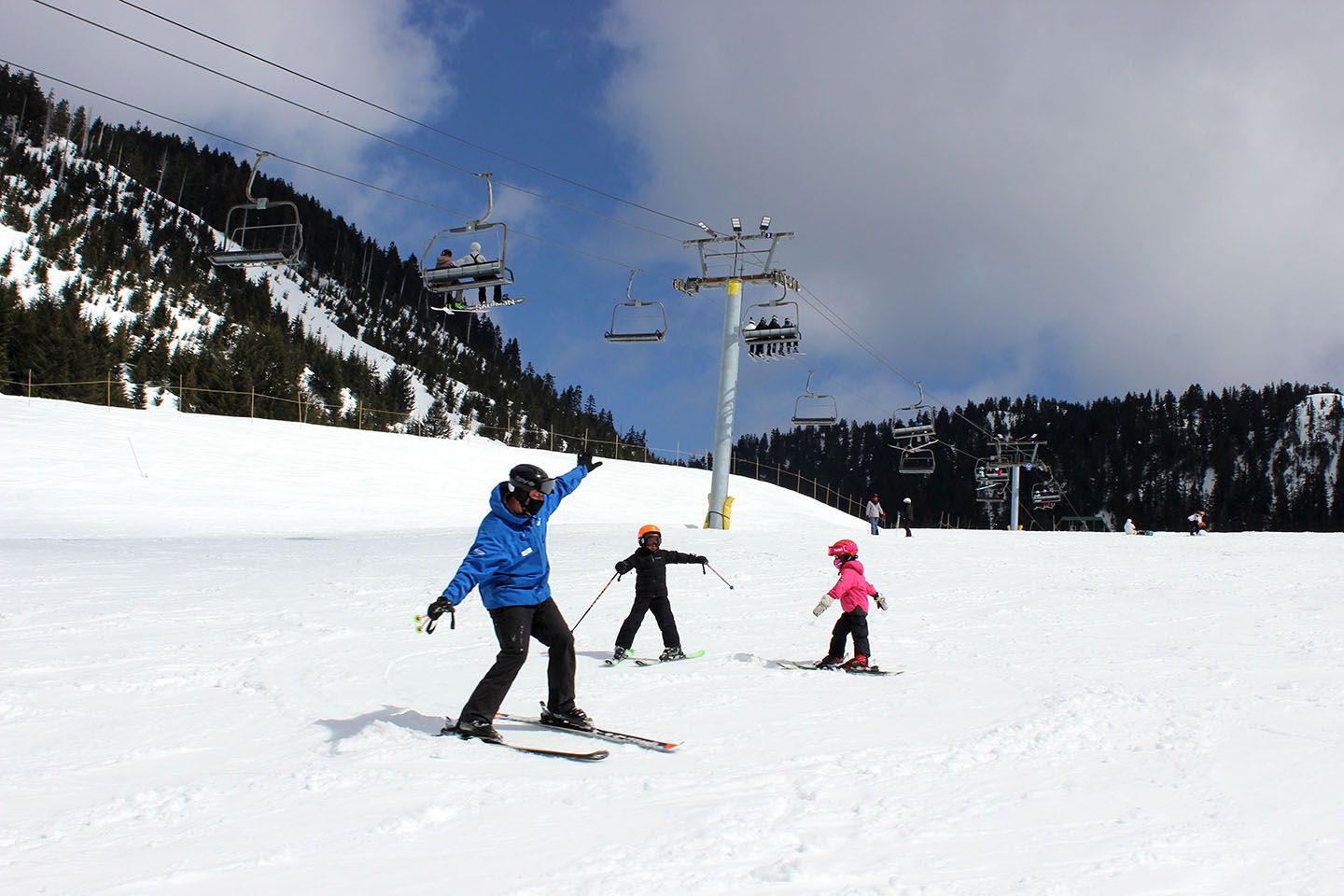 Ski instructor teaching two kids in front of chairlift.