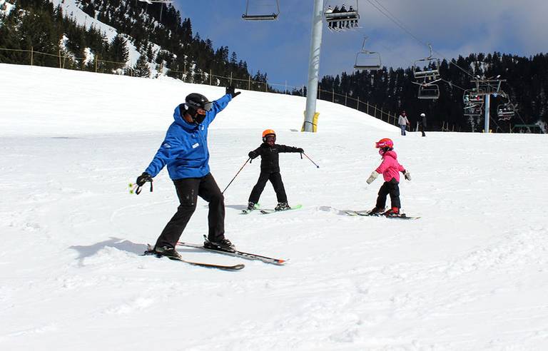 Ski instructor teaching two kids in front of chairlift.
