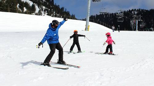 Ski instructor teaching two kids in front of chairlift.