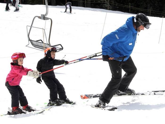 An instructor pulling two kids on skis.