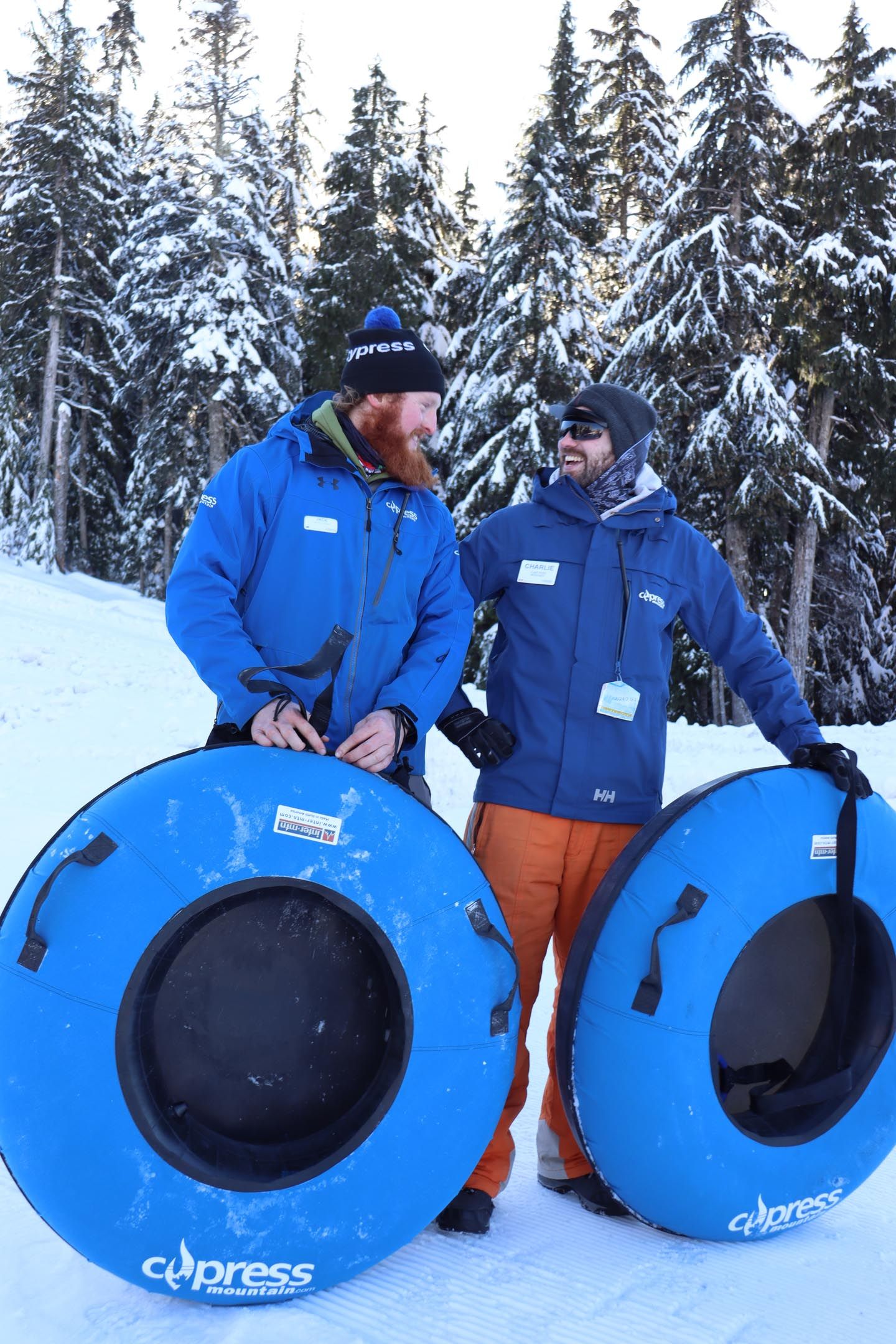 Two tubing staff looking and smiling at each other with snow tubes in their hands.