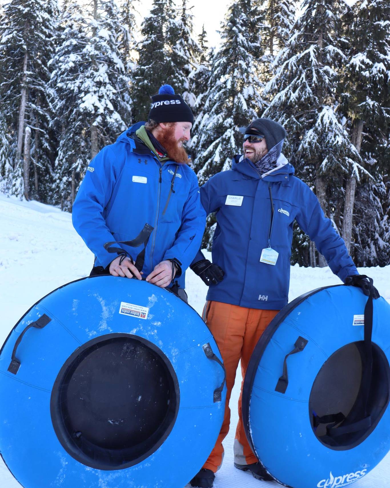 Two tubing staff looking and smiling at each other with snow tubes in their hands.
